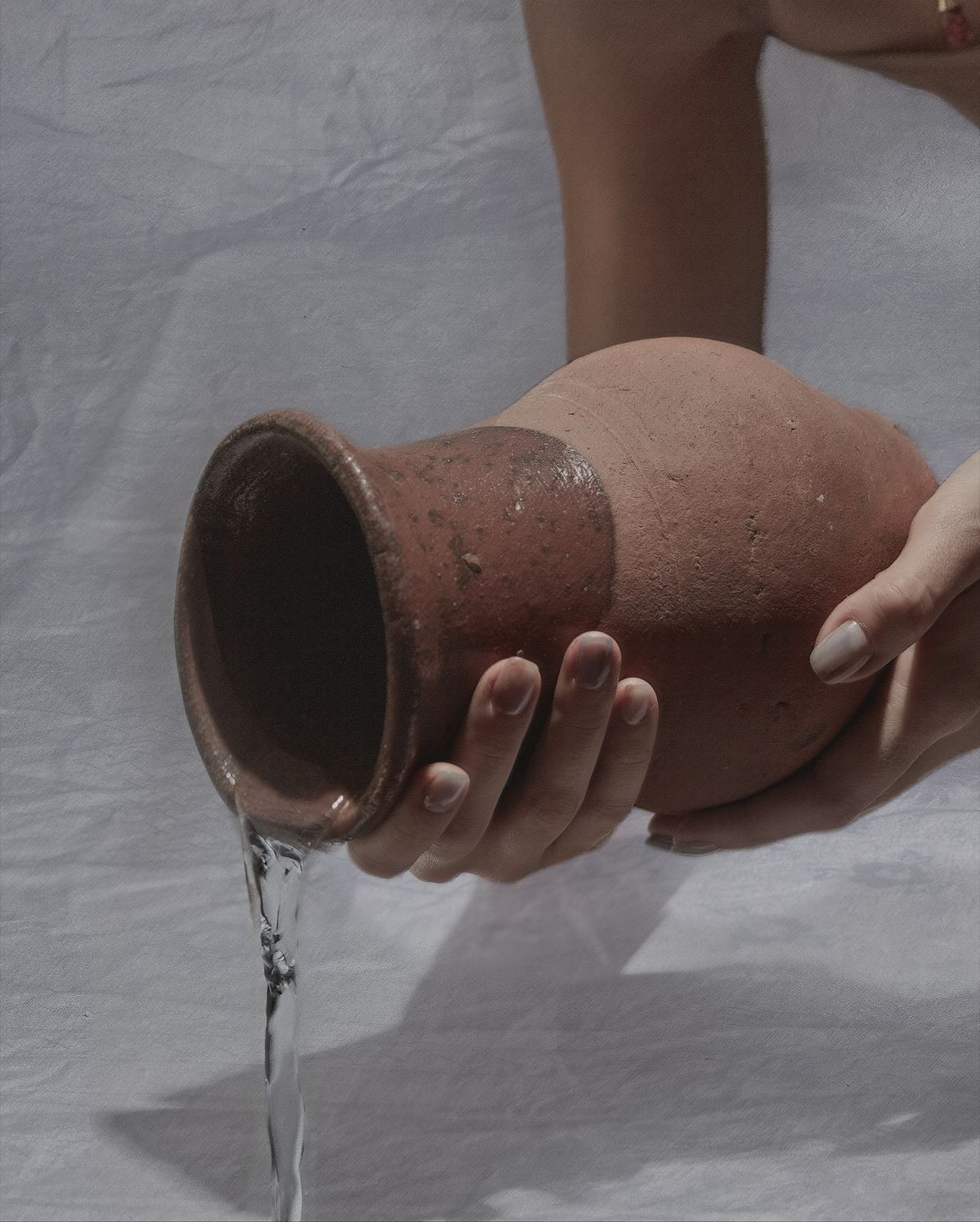 Hands pouring water from a clay jug